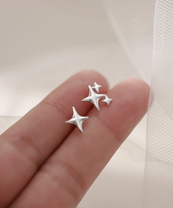 Macro shot of silver four-pointed star stud earrings on a fingertip for size scale