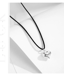Detail of silver heart pendant with black cord on white curved paper backdrop