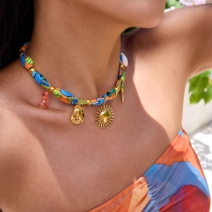 Detail of colorful woven necklace with 18K gold charms, shell and stones in resort style
