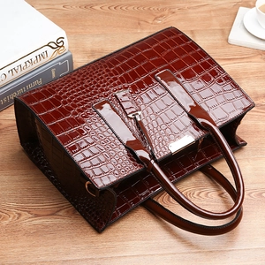 Dark brown crocodile pattern patent leather handbag on a wooden desk with a coffee cup
