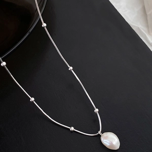 Close-up of silver bead chain necklace featuring a baroque white pearl pendant on black