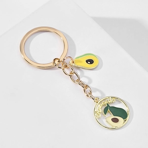 Close-up of golden metal avocado keychain with enamel details and cutout lettering