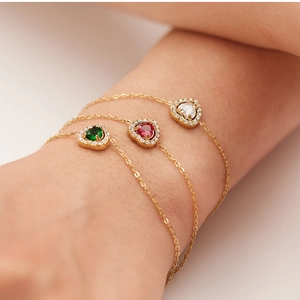 Detailed view of gold heart bracelets with green, pink, and white zircons on a model's wrist