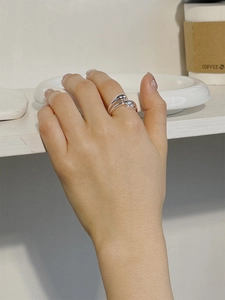 Close-up of minimalist S925 sterling silver drop wrap ring worn on finger in a cozy cafe