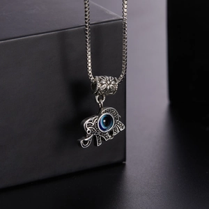 Close-up of silver elephant pendant with blue evil eye on black box background