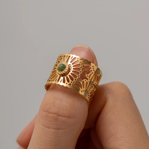 Detailed view of hollow floral pattern ring with green gemstone on thumb