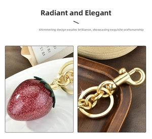 Detail of red glitter strawberry keychain with gold lobster clasp on white dish