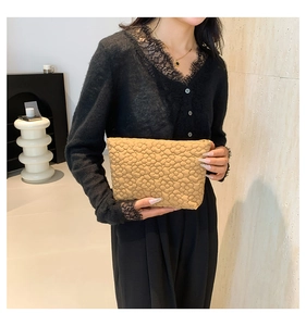 Detail of a khaki quilted floral clutch bag held by a model in a minimalist interior