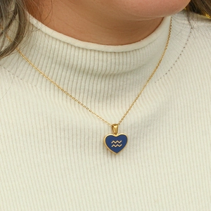Detail of gold Aquarius zodiac heart pendant worn on white sweater for women