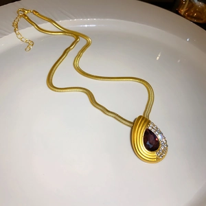 Detailed view of a gold snake chain necklace with a rhinestone drop pendant in a white dish