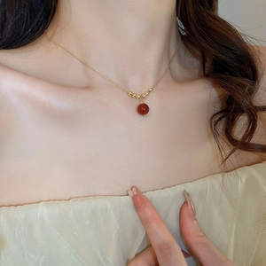 Detail einer vergoldeten Halskette mit rotem Perlenanhänger am Hals des Models