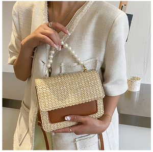 Close-up of woven straw handbag featuring faux pearl handle and brown leather flap detail