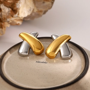Detail view of 18k gold and silver X-shaped criss-cross stud earrings on ceramic