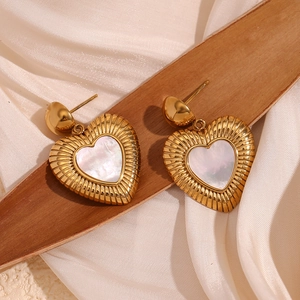 Détail macro de boucles d'oreilles cœur en or 18K avec nacre blanche sur bois et soie