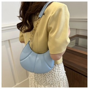 Light blue shell-shaped shoulder bag with gold chain strap shown on a model's shoulder