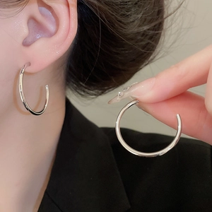 Macro view of minimalist silver C-shaped hoop earring worn on ear for size reference