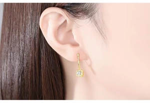Close-up of gold square drop earrings with pavé set crystals and central diamond on model
