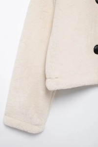 Detailed close-up of cream faux fur sleeve joint and contrasting black button finish