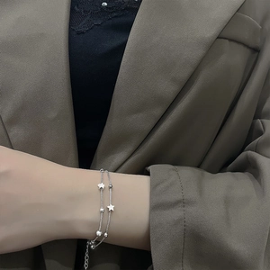 Close-up of double-layer silver star and bead bracelet worn on wrist over a brown blazer