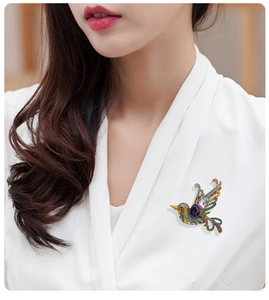 Close-up of a vintage rhinestone bird brooch on a white blazer, colorful crystal jewelry