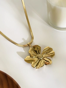 Detail of a large golden flower pendant necklace featuring a delicate snake chain