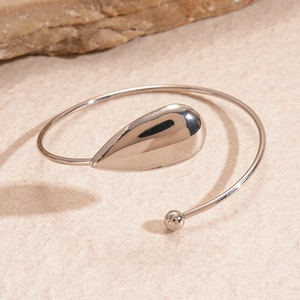 Gros plan détaillé d'un bracelet ouvert en argent poli en forme de goutte sur fond sable