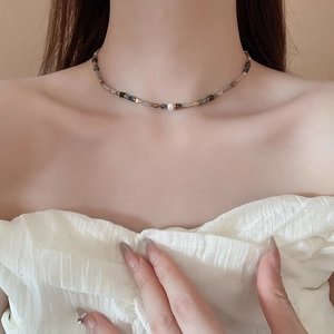 Detail of beaded necklace featuring gray faceted beads and a baroque pearl on collarbone
