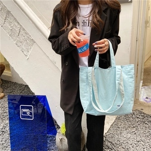Detalle del bolso de lona azul claro con correa de cuadros azules y blancos en entorno urbano