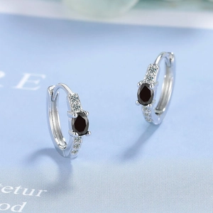 Macro shot of silver huggie earrings with oval black zircon and clear stone accents