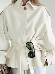 Detailed view of cropped cream trench coat featuring lapels, epaulettes and waist tie