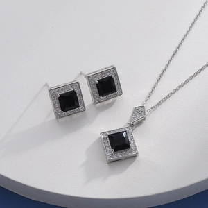 Macro detail of silver necklace and earrings set with square black gems and zircon halo