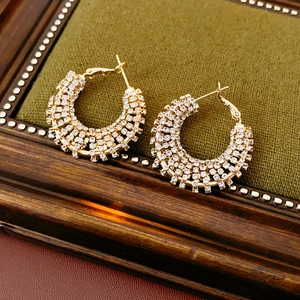 Macro shot of gold-tone round hoop earrings with sparkling crystal pavé on green fabric
