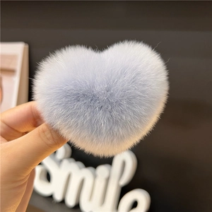 Detail of soft heart-shaped light blue faux fur hair clip held by a hand close-up view