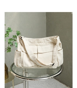 Detail of a minimalist cream canvas crossbody bag featuring functional external pockets