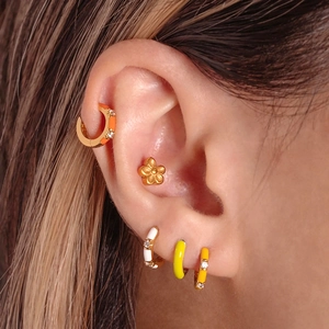 Macro detail of colorful enamel bamboo hoop earrings and gold floral stud worn by model