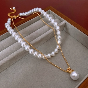 Détail d'un collier de perles double épaisseur avec pendentif doré en écrin gris