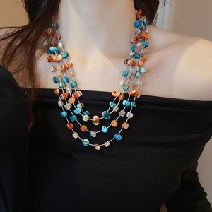 Detail of layered irregular blue and orange shell bead necklace on a model