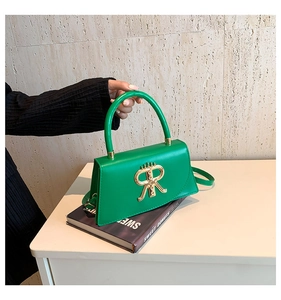 Detail of green handbag with gold R-shaped ornament and handle placed on a book