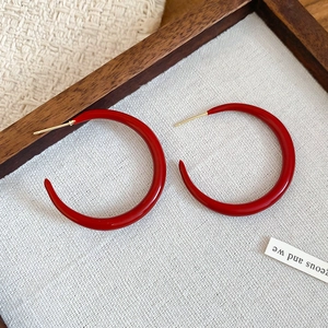 Detailed close-up of glossy red C-shaped hoop earrings with gold-tone studs and premium finish
