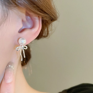 Vue détaillée de boucles d'oreilles nœud argenté avec perles blanches sur l'oreille