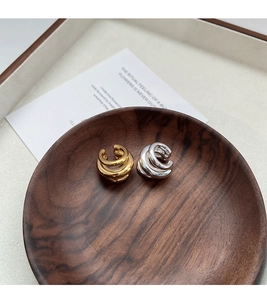 Detail of minimalist gold and silver tiered C-shaped ear cuffs on a wooden tray