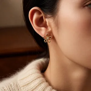 Golden hollow flower stud earrings with shimmering zircon centers on a model wearing knitwear