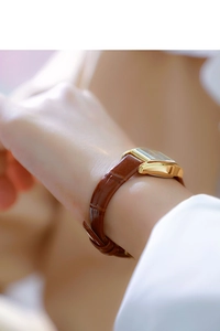 Close-up of elegant gold rectangular watch with brown leather strap on a wrist