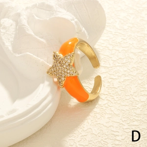 Close-up of adjustable gold star ring featuring orange enamel and sparkling zircons