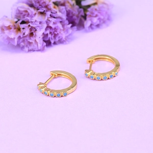 Macro detail of gold hoop earring with turquoise stones on lavender background