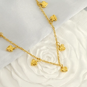 French style golden stainless steel necklace with heart pendants on white fabric background