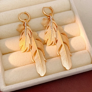 Detail view of gold feather hoop earrings with pavé crystals in a cream jewelry box