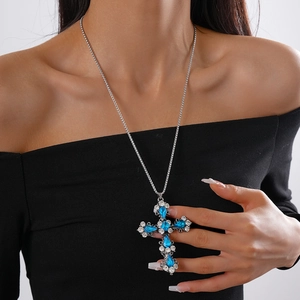 Detailed view of luxury cross pendant necklace with blue crystal on model neck