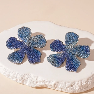 Macro shot of flower earrings with blue and purple crystals on a textured stone