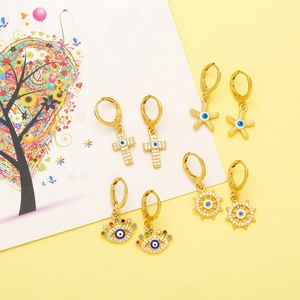 Detail of four gold earrings featuring cross, starfish, evil eye and rudder designs
